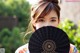 A woman holding a black fan in front of her face.