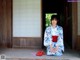 A woman in a kimono sitting on the porch of a house.