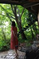 A woman in a red dress standing in front of a tree.