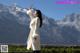 A woman in a white coat standing in front of a mountain range.