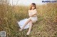 A woman in a white dress sitting in a field of tall grass.